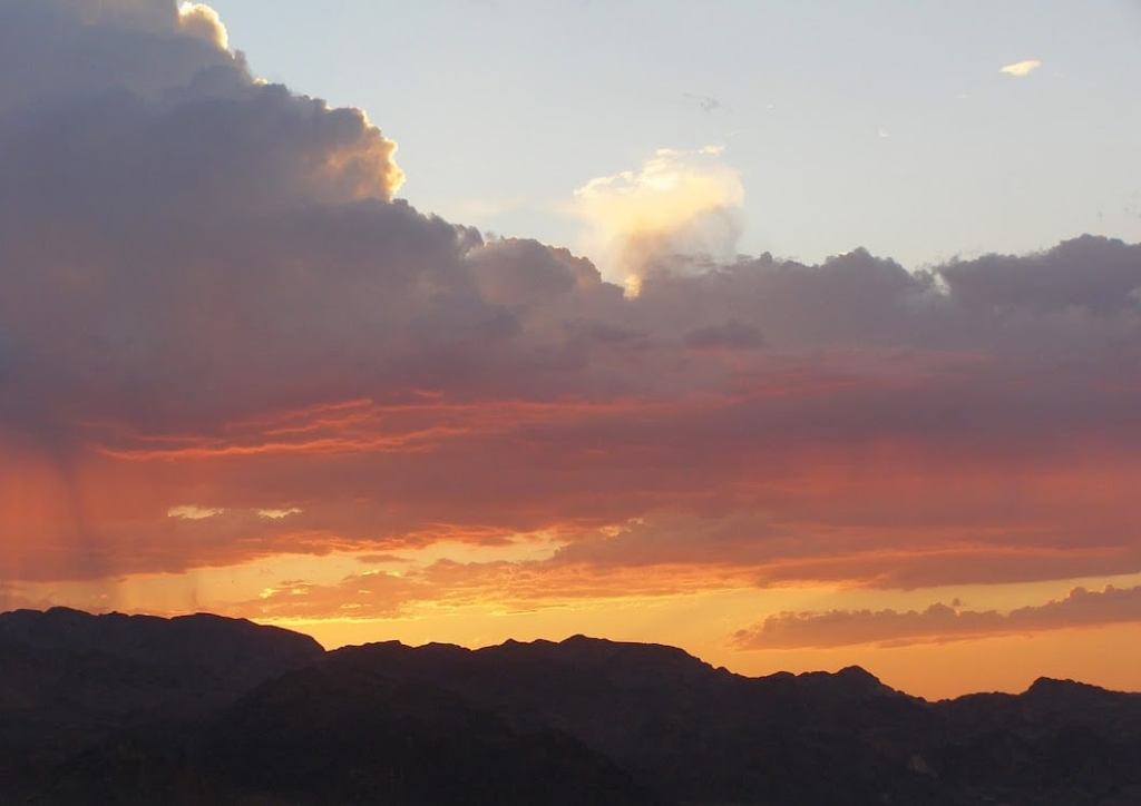 Orange sunset behind mountains with the sun still lighting up the sky above a cloud layer, showing a brilliant, light blue sky at the top.